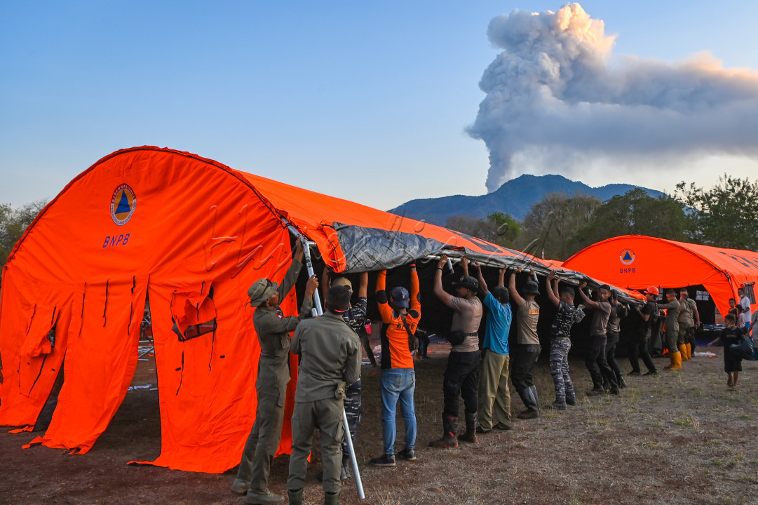 Sejumlah petugas BNPB, TNI, Polri, dan warga mendirikan tenda untuk pengungsi terdampak erupsi Gunung Lewotobi Laki-laki di posko yang baru didirikan di Desa Kobasoma, Titehena, Kabupaten Flores Timur, Nusa Tenggara Timur, Minggu (10/11/2024). BNPB memperluas sebaran tempat pengungsian untuk menampung semua warga korban terdampak erupsi Gunung Lewotobi Laki-Laki yang jumlahnya semakin bertambah, sementara pos-pos pengungsi yang telah berdiri sebelumnya sudah tidak mampu lagi menampung setelah radius zona bahaya erupsi diperluas menjadi sembilan kilometer di sektor barat daya-barat laut dan tujuh kilometer dari puncak kawah.&nbsp;