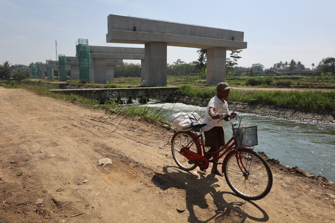 Petani melintas di lokasi pembangunan Jalan Tol Yogyakarta - Bawen Seksi 1 di tepi Selokan Mataram, Kecamatan Tempel, Sleman, DI Yogyakarta, Jumat (19/7/2024). Jalan Tol Yogyakarta - Bawen sepanjang 76,30 Km merupakan bagian dari Proyek Strategis Nasional (PSN) yang dibagi dalam enam seksi. Seksi 1 Sleman-Banyurejo sepanjang 8,25 Km ditargetkan selesai pada awal 2025.&nbsp;